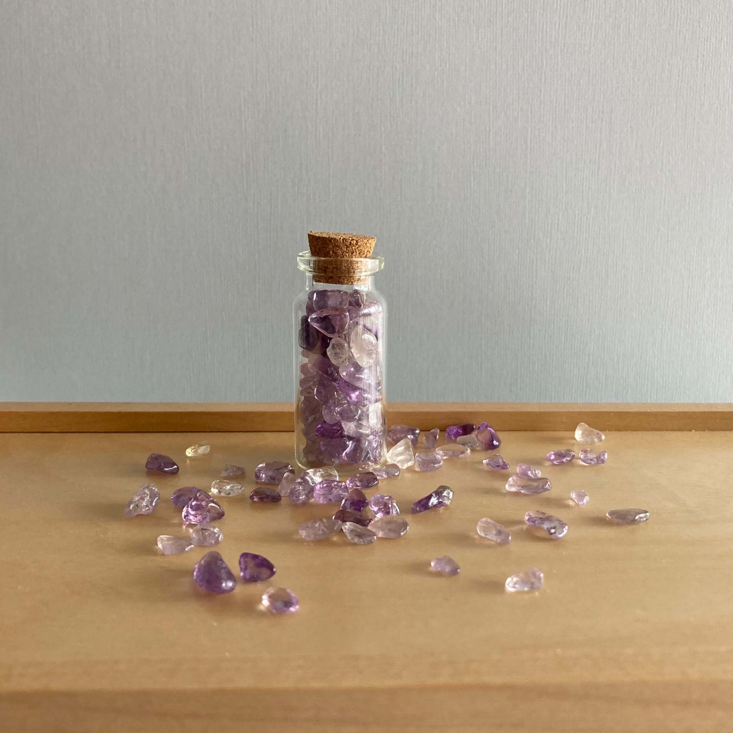 Small bottle of Amethyst chips on a wooden box surrounded by loose Amethyst chips